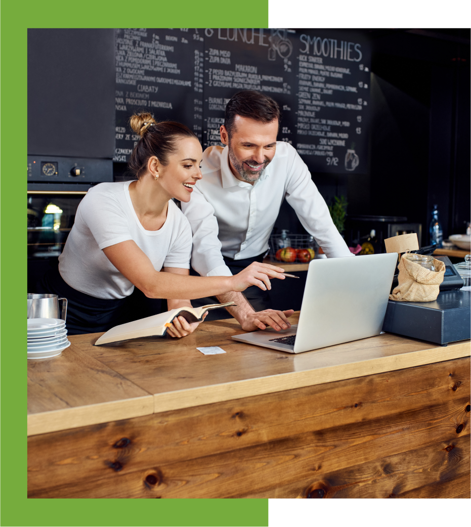 Two people are looking at a laptop in front of the counter.